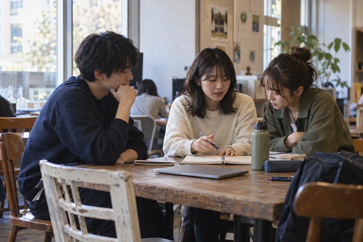 机を囲み、ノートを見ながら企画を相談する学生たちのイメージ
